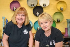 Karen and Swooz pose in front of a color wheel display of Black Dog Salvage furniture paint