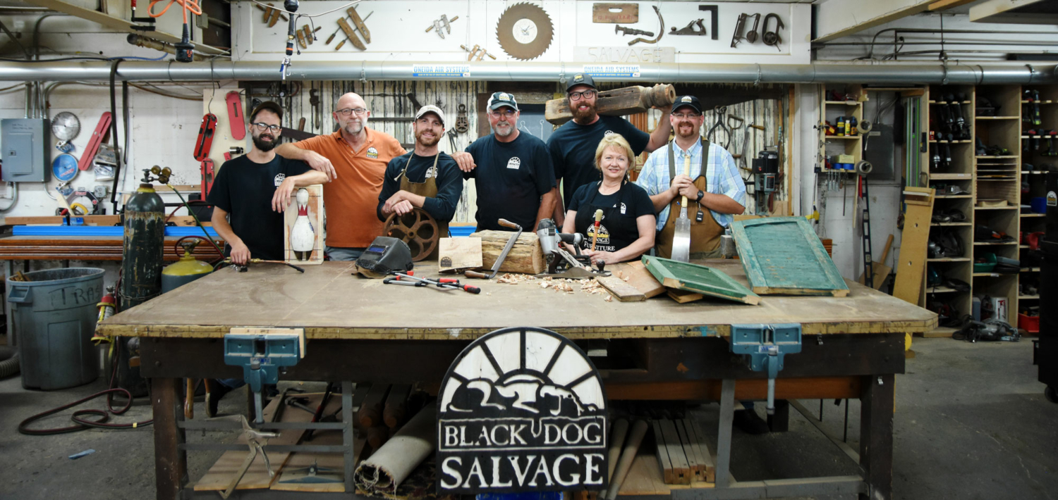 Salvage Dawgs crew stand behind a work bench in the Black Dog Salvage shop